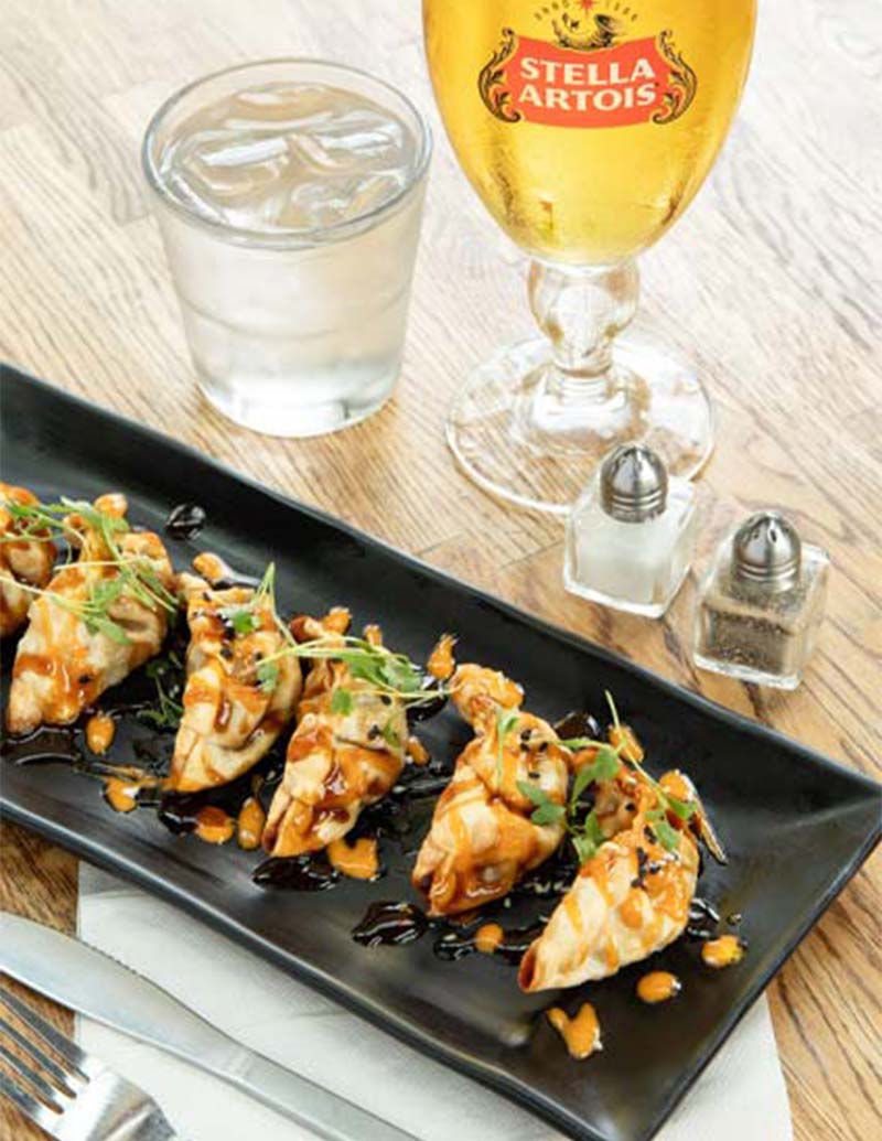 A plate of dumplings with sauce, Stella Artois, and water featured in Southpointe PA Magazine.